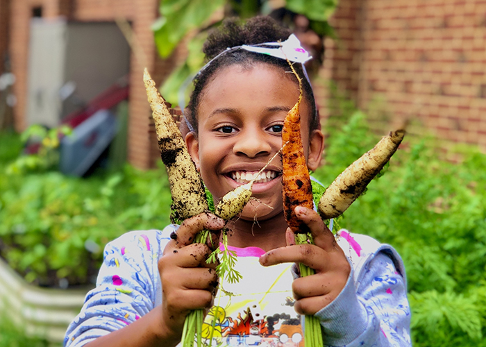 Smiling girl with freshly harvested carrots shows the lasting impact of FoodPrints 