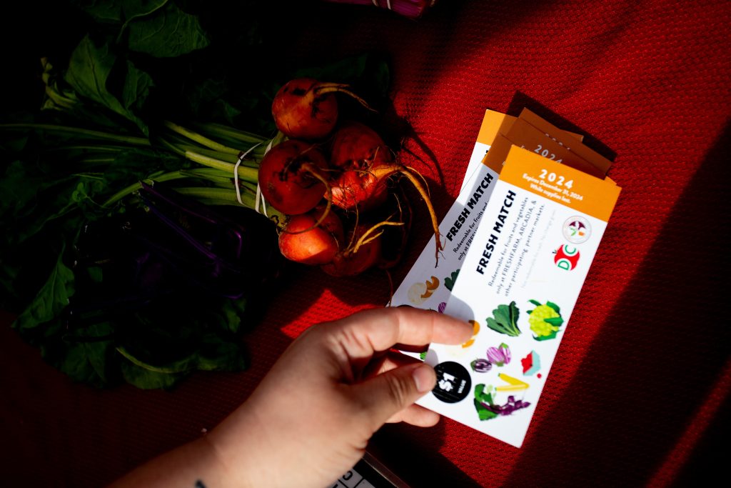 Hands reach to set white FRESHMATCH coupons on a table. A bunch of beets sits on the table.